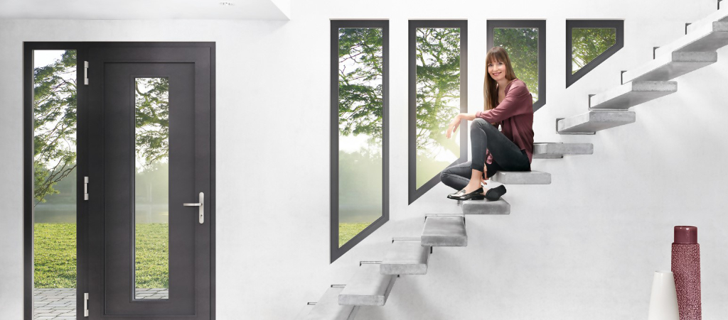 Eine Frau sitzt auf einer Treppe vor Fenster mit dunklem Rahmen. Die Tür ist dem Design der Fenster angeglichen | Daldrup Fenster